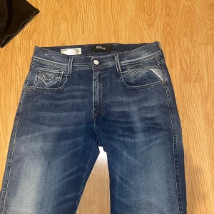 Blå jeans Replay Anbass herr - Snygga blå jeans från Replay, modell Anbass. Klassisk femficksdesign med ljusa slitningar och kontrastsömmar. Jeansen har normal midja och raka ben. Tillverkade i stretchigt denim för extra komfort. Perfekta för en avslappnad och trendig stil.
