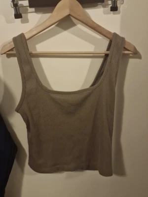 Ribbad beige linnetopp - Snygg ribbad linnetopp i beige med breda axelband och croppad passform. Perfekt att matcha med jeans eller kjol för en trendig look. Mjuk och stretchig känsla.