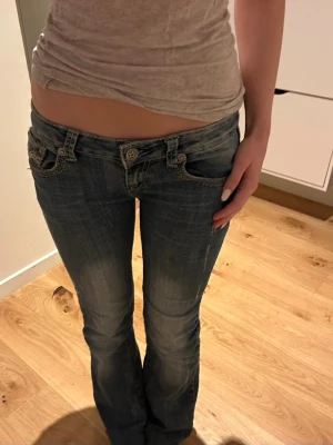Låga bootcut jeans i blå denim - Snygga blå bootcut jeans med låg midja och slitningar framtill. Jeansen har klassiska fem fickor och markerade sömmar. Perfekta för en avslappnad och trendig look. Materialet är denim med lätt stretch för skön passform.