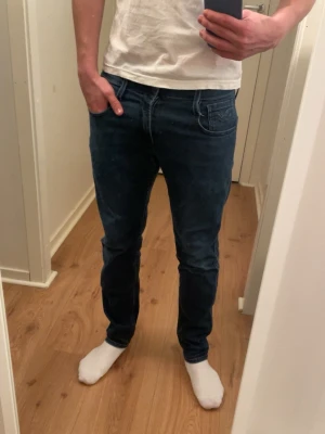 Mörkblå slim fit jeans herr - Snygga mörkblå slim fit jeans med klassisk femficksdesign och normal midja. Jeansen har en stilren look och sitter tajt längs benen. Perfekta för dig som gillar en modern och enkel stil.