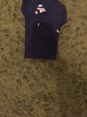 Mörkblå pikétröja från Abercrombie - Klassisk mörkblå pikétröja från Abercrombie & Fitch med korta ärmar och knappslå framtill. Liten broderad logga på bröstet. Perfekt till jeans eller shorts för en avslappnad look.