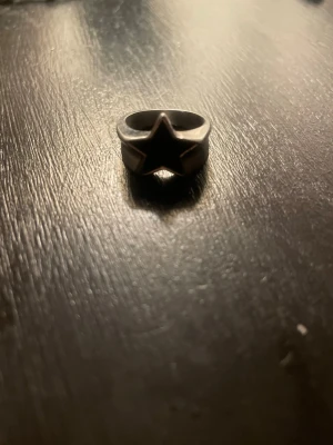 Svart ring med stjärnform - Cool ring i svart metall med en tydlig stjärnformad design framtill. Ringen har en robust känsla och passar perfekt för dig som gillar unika accessoarer med attityd. Från Punktshop.