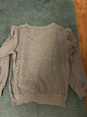 Grå sweatshirt från Polo Ralph Lauren - En stilren grå sweatshirt från Polo Ralph Lauren i mjuk bomullsmix. Klassisk rund halsringning, långa ärmar och broderad logga på bröstet. Perfekt för en chill och avslappnad look.