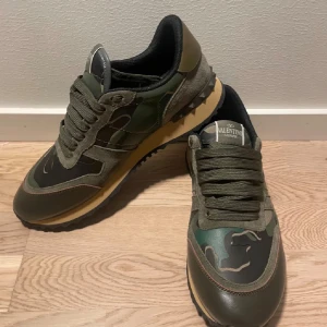Valentino Garavani Rockrunner sneakers - Snygga Valentino Rockrunner sneakers i mörkgrön och svart med camouflage-mönster. Skorna har snörning, platt sula och detaljer i mocka och skinn. Ikonisk logga på plösen och innersulan. Perfekt för dig som gillar exklusiva streetwear-vibbar. Sprillans nya 