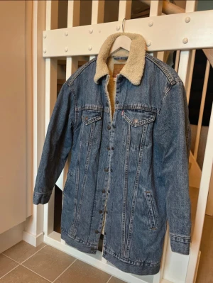 Levi's jeansjacka med teddyfoder XS - Säljer en Levi's Premium jeansjacka i blå denim med mjukt teddyfoder och krage i beige. Jackan har klassiska bröstfickor med knappar, sidofickor och knappstängning framtill. Perfekt för dig som gillar street och vintage-vibe.