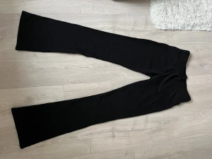 Svarta bootcut mjukisbyxor - Svarta mjukisbyxor med bootcut-modell och låg midja. De har en klassisk och stilren look med utsvängda ben. Perfekta för dig som gillar en enkel men trendig stil. Materialet känns mjukt och stretchigt, vilket gör dem bekväma att bära hela dagen.