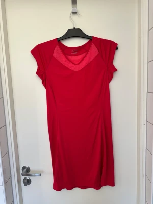 Röd sportklänning från Arc'teryx - Snygg röd kortklänning från Arc'teryx med sportig design och meshdetaljer vid halsringningen och ryggen. Klänningen har en praktisk ficka med dragkedja på ryggen och är tillverkad i lätt syntetmaterial som andas. Perfekt för aktiva dagar och träning.