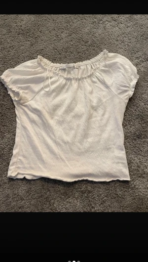 Vit croppad blus från 157 XS - Säljer en söt vit blus från 157 i storlek XS. Toppen är croppad med korta puffärmar och har en rynkad halsringning med liten knyt-detalj. Materialet är mjukt och lätt, perfekt för varma dagar. Enkel och stilren design som är lätt att matcha.