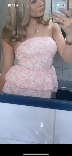 Rosa axelbandslös topp - Supersöt axelbandslös topp i ljusrosa med vitt blommönster och volangdetalj i midjan. Knytning i ryggen, skriv vid intresse av bilder