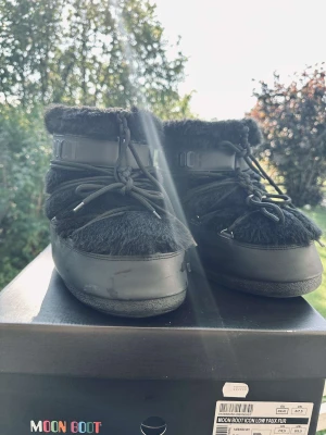 Svarta Moon Boot Icon Low Faux Fur (kan diskuteras om pris) - Moon Boot Icon Low Faux Fur i svart med fluffig fuskpäls och snörning runt skaftet. Bootsens platta sula och rundade tå gör dem både sköna och snygga. Perfekta för vinter och kalla dagar, med cool design och tydlig logga på skaftet.