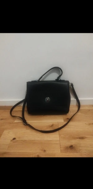 Svart axelväska i skinn med silverdetaljer - En svart väska är enkel och stilren, perfekt till alla outfits. Inuti finns många olika fack där man kan lägga och organisera sina saker, så allt hålls på plats och är lätt att hitta.