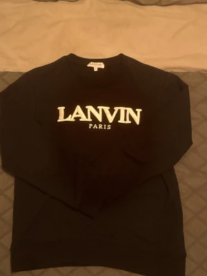 Lanvin tröja  - Svart sweatshirt från Lanvin Paris i storlek L  PASSAR M perfekt. Tröjan har ett stort vitt Lanvin Paris-tryck på bröstet och klassisk rund hals. Mjuk och skön bomullskvalitet med långa ärmar och ribbade muddar. Perfekt för dig som gillar stilrena designer och exklusiva märken.