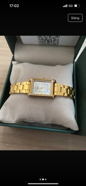 Casio guldfärgad fyrkantig klocka - Snygg guldfärgad klocka från Casio med fyrkantig boett och länkarmband i metall. Urtavlan är vit med guldiga detaljer och siffror, vilket ger en clean och klassisk look. Perfekt för dig som gillar stilrena accessoarer med lite lyxig känsla.