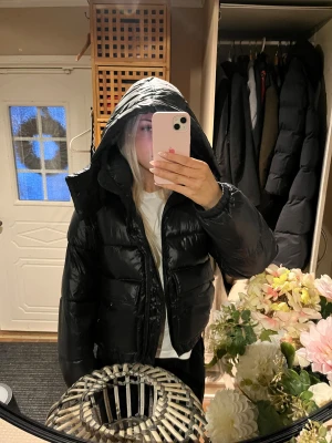 Svart pufferjacka från Weekday XS - Säljer en svart pufferjacka från Weekday i storlek XS. Jackan har en stor huva, dragkedja framtill och är quiltad med breda kanaler. Materialet är glansigt syntet och jackan har en loose passform som ger en cool och avslappnad vibe.