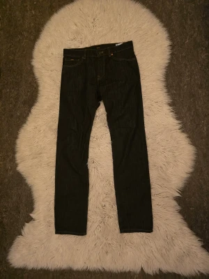 Mörkblå jeans från BOSS Maine storlek 32/34 - Snygga mörkblå jeans från BOSS, modellen Maine. Klassisk femficksdesign med kontrasterande orange sömmar och rak passform. Jeansen har normal midja och är tillverkade i slitstarkt denimtyg. Perfekt för dig som gillar stilrena och tidlösa jeans.