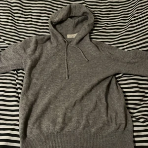 Grå cashmere hoodie från Sayless XXS - Mjuk och lyxig grå hoodie från Sayless i äkta cashmere. Tröjan har huva med snörning, långa ärmar och bred ribbad kant nedtill. Perfekt för dig som gillar chill och stilren look. Designad i Sverige och i storlek XXS. Nypris ligger runt 899