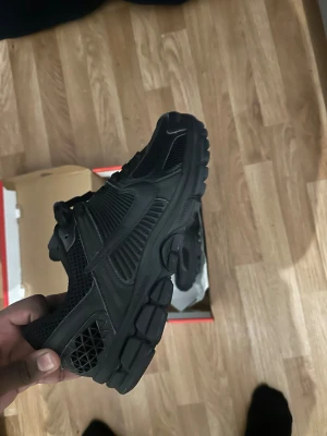 Svarta Nike vomero  - Säljer ett par helsvarta Nike sneakers med chunky sula och snygga detaljer i mesh och skinn. Skorna har snörning och en sportig vibe, perfekta för dig som gillar streetwear. Swoosh-loggan syns tydligt på sidan och designen är riktigt clean.