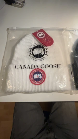 Vit ribbad mössa från Canada Goose - Pris kan diskuteras. Snygg ribbad vit mössa från Canada Goose med klassisk logopatch framtill i rött, blått och vitt. Märket är broderat. Mössan håller dig varm vilket är perfekt nu för vintern. 