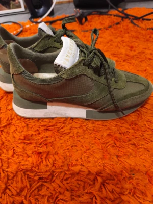 Olivgröna sneakers från Pavement - Snygga olivgröna sneakers från Pavement med cool retrostil. Ovandel i mocka och textil, vita detaljer på tungan och mellansulan. Skorna har snörning och platt sula, perfekt för en avslappnad streetlook. Snygga detaljer och bekväm passform.