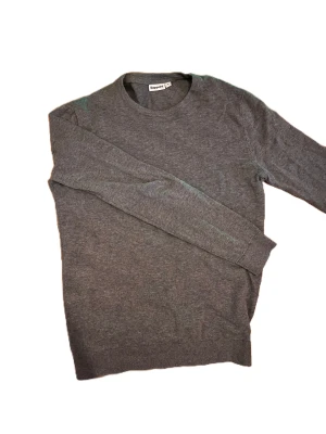 Grå tröja från Kappahl - En enkel och stilren grå tröja från Kappahl i storlek S. Tröjan har rund halsringning och långa ärmar, perfekt för lager-på-lager under kyligare dagar. Mjuk och skön känsla som passar till allt.