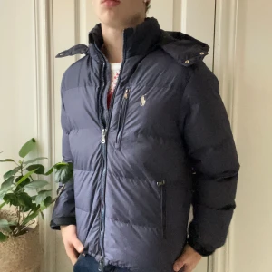 Ralph lauren dun jacka - Ralph lauren dun jacka, en hur skön jacka som helst med riktigt najs passform! Inga defekter och modellen är 180 cm 75 kg och bär storlek M. Färgen är mörkblå / svart skulle jag säga. Kom med frågor! Man kan spänna åt i midjan om man vill att den ska sitta mer tight 🙌
