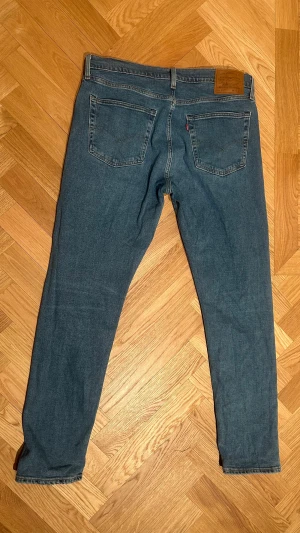 Levi's 512 blå jeans W36 L32 - Säljer ett par Levi's 512 jeans i klassisk blå färg. Modellen har raka ben och fem fickor, med den ikoniska läderpatchen bak i midjan. Jeansen är tillverkade i denim och har en snygg, tidlös look som funkar till det mesta.