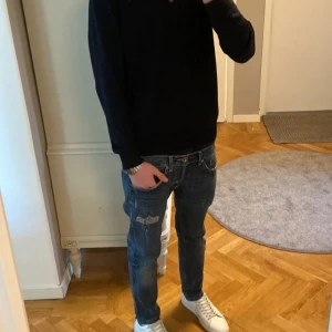 Blå Dondup jeans med slitningar - Snygga blå jeans från Dondup med coola slitningar och detaljer med färg splatter på både fram- och baksida. Klassisk femficksmodell med kontrastsömmar och låg midja. Jeansen har en rak passform och är tillverkade i mjukt denimtyg för skön känsla. Storlek W29 L30