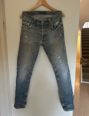 Nudie Jeans Grim Tim grå jeans 32/32 - Säljer ett par Nudie Jeans Grim Tim i tvättad gråblå färg i en snygg sliten look. Modellen har slim passform och klassisk femficksdesign. Jeansen är tillverkade i  bomull. Perfekt för dig som gillar en avslappnad stil.                                       Skriv om ni har frågor.                                            Pris kan diskuteras!