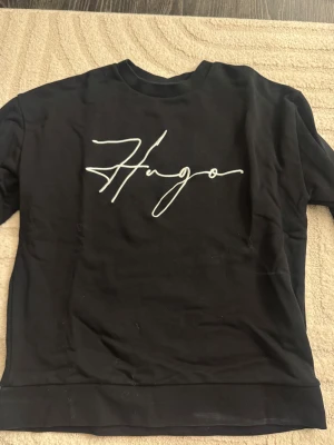 Svart sweatshirt med tryck - Svart sweatshirt från Hugo Boss (äkta). Använd några gånger, säljer därav har ingen användning för den.  Nypris 1300kr