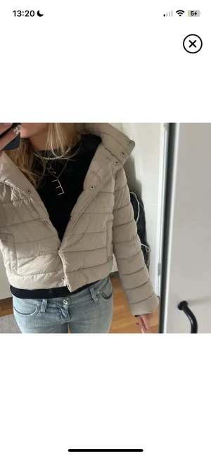 Beige croppad herno liknande jacka - Säljer en beige pufferjacka med croppad passform och huva. Jackan har quiltad design, långa ärmar och knappar framtill. Perfekt för dig som gillar en chill och trendig look under höst och vinter. Fickor på sidorna och snygg, enkel stil.💞💞
