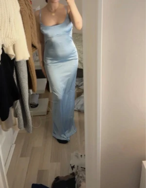 Ljusblå klänning  - Säljer en elegant ljusblå långklänning med smala axelband och snygg öppen rygg. Klänningen har en figurnära passform och är gjord i ett glansigt satinliknande material som ger en lyxig känsla. Perfekt för dig som vill sticka ut nu under sommaren 😍 endast testad 