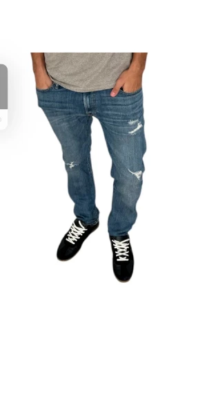 Blå Abercrombie & Fitch Langdon Slim jeans - Säljer ett par blå Langdon Slim jeans från Abercrombie & Fitch med stretch. Jeansen har slitna detaljer på framsidan, klassisk femficksdesign och brunt läderpatch med A+F bak. Passformen är slim och materialet är jeans.