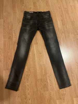 Replay Anbass Hyperflex Jeans - Svarta Replay Anbass Hyperflex jeans i slim fit med snygga slitningar och klassiska fem fickor. Stretchigt material som sitter skönt och följer kroppen. Bakfickorna har coola broderade detaljer och jeansen har en modern, smal siluett. Otroligt fräscha