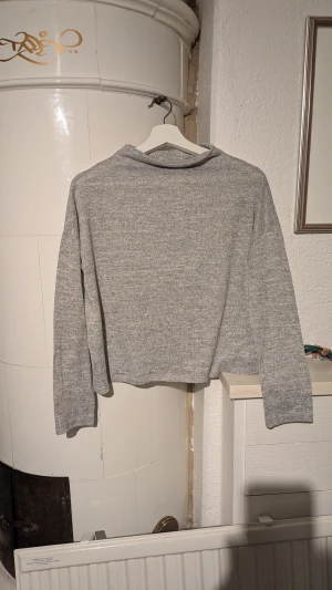 Grå croppad stickad tröja - Snygg grå croppad stickad tröja med lång ärm och enkel design. Perfekt för dig som gillar en chill och stilren look. Mjuk och skön känsla, passar till jeans eller kjol. Tröjan har en rak passform och är lätt att matcha med andra plagg.