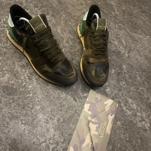 Valentino Rockrunner i camouflage - Snygga Valentino Rockrunner sneakers i ett coolt camouflage-mönster. Skorna har en kombination av mocka och skinn med snörning framtill. Skorna har en lite defekt på höger skon, inget man ser när man har de på. Priset är ej hugget i sten. Buda på!