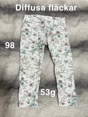 Blommiga leggings från Newbie  - Supersöta leggings från Newbie i vitt med blommigt mönster i lila, grönt och blått. Perfekta att matcha med en enkel topp eller hoodie.🌸 Diffusa fläckar. Storlek 98