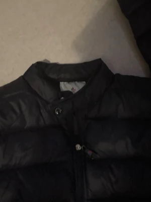 Svart Moncler pufferjacka M - Säljer en svart pufferjacka från Moncler i storlek M. Jackan har klassisk quiltad design, hög krage och dragkedja framtill. Moncler-logga på bröstet ger en clean och exklusiv look. Perfekt för kalla dagar och riktigt snygg till streetwear.