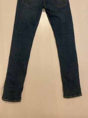 Jack & Jones Slim Glenn blå jeans - Säljer ett par mörkblå jeans från Jack & Jones, modell Slim Glenn. Jeansen har klassisk femficksdesign, smal passform och snygga kontrastsömmar. Tillverkade i slitstarkt denim med metallnitar och knappgylf.