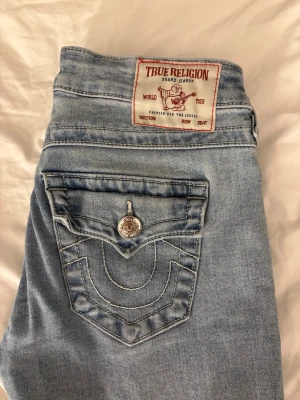 True Religion Joey Low Rise Flare Jeans - Snygga ljusblå jeans från True Religion, modell Joey Low Rise Flare. Klassiska fickor med lock och silverfärgade knappar med logga. Tydliga kontrastsömmar och ikonisk patch bak. Skicka om ni vill ha fler bilder eller har frågor!!💗