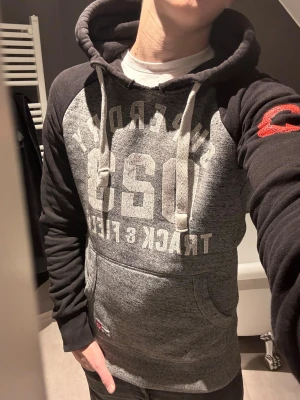 Vintage superdry hoodie - Rikigt fet superdry hoodie i svart och grå. Väldigt härlig passform, luvan satt även väldigt fint! Den är i storlek S och modellen är 183,75 kg. Den satt lite väl tight så skulle passa folk som väger lite mindre, men de beror ju förstås på hur du vill att den ska sitta! Väldigt fint skick och denna är svår att få ta på, speciellt i denna coulorway👌pris kan diskuteras
