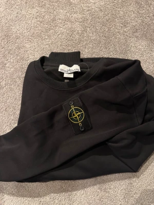 Svart Stone Island sweatshirt - Svart sweatshirt från Stone Island med loggan på sidan av armen, väldigt bra skick då jag knappt använt den då den är för liten för mig. Den är i storlek M men sitter mer som en S