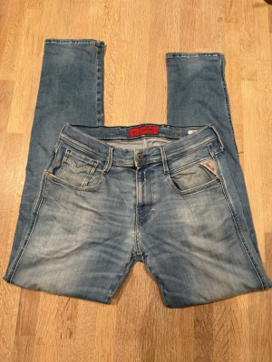 Replay Anbass ljusblå jeans, W29 L30 - Säljer ett par Replay Anbass jeans i ljusblå tvätt med snygga slitningar och klassiska fem fickor. Modellen har normal passform och raka ben. Tydliga Replay-detaljer med röd logga på myntfickan och patch bak i midjan. Perfekta till en avslappnad stil.