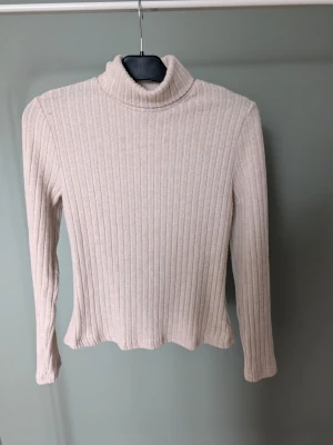 Beige ribbad polotröja - Mysig beige polotröja från SHEIN i storlek M. Tröjan är ribbad, har lång ärm och hög krage som ger en clean och stilren look. Perfekt att styla med jeans eller kjol för en enkel men snygg outfit.