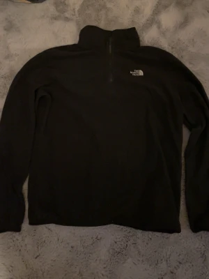Svart fleece half zip från The North Face - Säljer en svart fleece från The North Face i storlek L. Tröjan har half zip, hög krage och logga på bröstet.