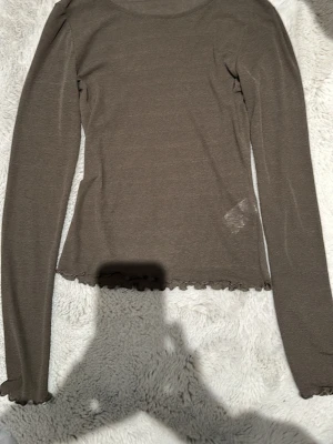 Mörk grön långärmad topp från BikBok - Säljer en tunn, mörk grön långärmad topp från BikBok i storlek XS. Toppen har volangkant vid ärmslut och nederkant, är figurnära och gjord i ett stretchigt, transparent material. Perfekt att styla med jeans eller kjol för en enkel men snygg look. Har fått hänga med ut från rensningen från min garderob. Har själv aldrig använt den utan bara hängt i min garderob 
