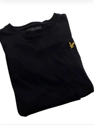 Mörkblå t-shirt från Lyle & Scott - Snygg mörkblå t-shirt från Lyle & Scott med klassisk gul logga på bröstet. Tillverkad i 100% bomull för skön känsla och enkel stil. Perfekt till jeans eller shorts för en clean look.