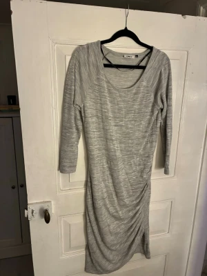 Grå långklänning från ONLY - Säljer en grå långklänning från ONLY i storlek XL. Klänningen har trekvartsärm, rund halsringning och snygg rynkning på sidan som ger en cool draperad effekt. Tillverkad i mjuk bomullsmix och har en enkel, stilren look som passar perfekt till sneakers eller boots. Skulle säga att den är liten i storlek o passar snarare M/L.