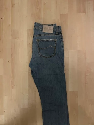 Blå jeans från Jacob Cohen modell  - Säljer ett par klassiska blå jeans från Jacob Cohen, modell PW610 Comfort. Jeansen är tillverkade i Italien av 99% bomull och 1% elastan för extra komfort. De har raka ben, snygga kontrastsömmar och en liten broderad J på myntfickan. Perfekta för dig som gillar stilrena och exklusiva jeans.