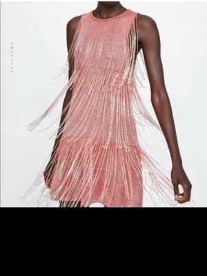 Glittrig rosa fransklänning ZARA - Supersnygg kort rosa klänning med glittrigt tyg och långa fransar som ger maxad partykänsla. Ärmlös modell med rund halsringning och en loose fit som känns både trendig och bekväm. Perfekt för dig som vill sticka ut!