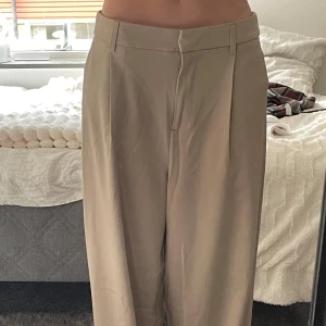 Beiga baggy kostymbyxor - Säljer ett par beiga kostymbyxor från Pieces i modellen PCPruisa LW Baggy Pants, köpta från Nelly. Byxorna har en loose och baggy passform, låg midja och vida ben.  Aldrig använda. Säljer då de inte passar.  Pris kan diskuteras.